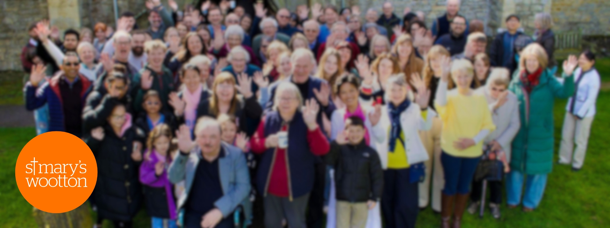 A group of church members, waving and smiling, standing in front of St Mary's church.